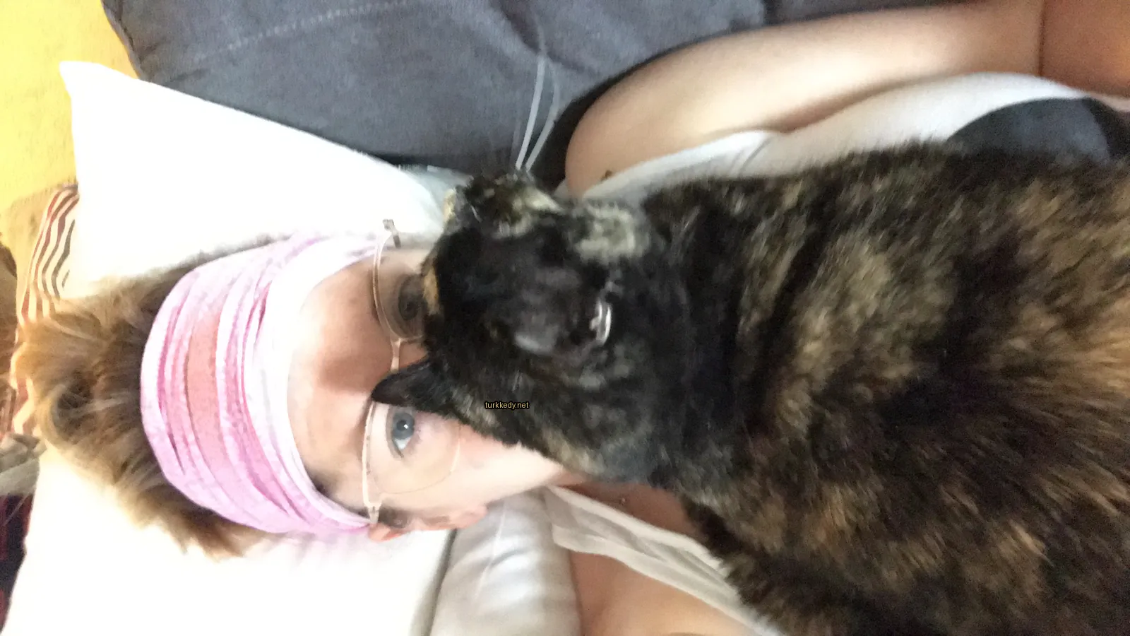 Kadının yüzüne yatan siyah ve kahverengi desenli bir kedi.
