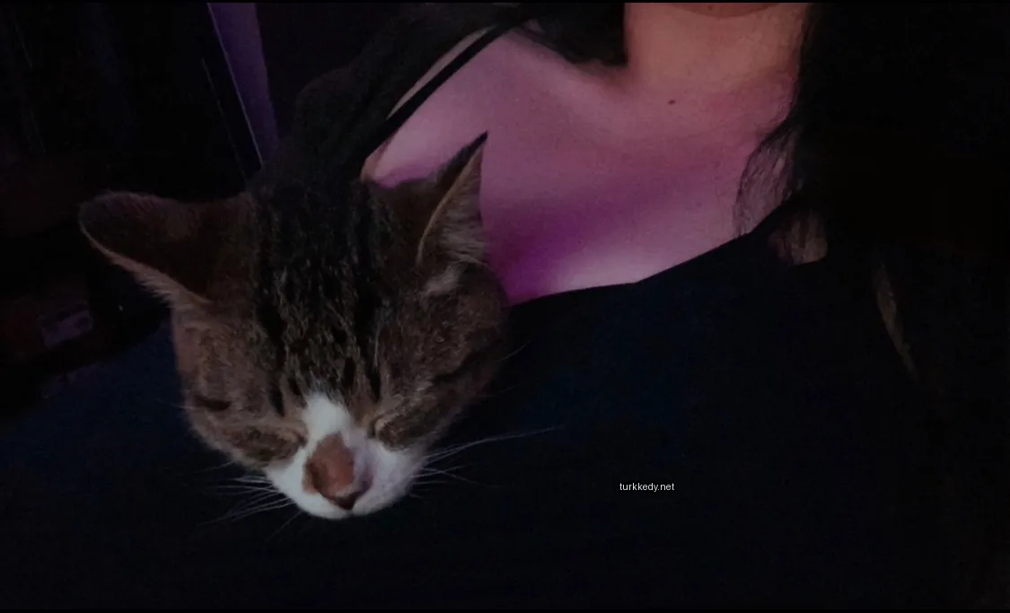 Kadının göğsünde bir kahverengi ve beyaz bir kedi uyuyor.